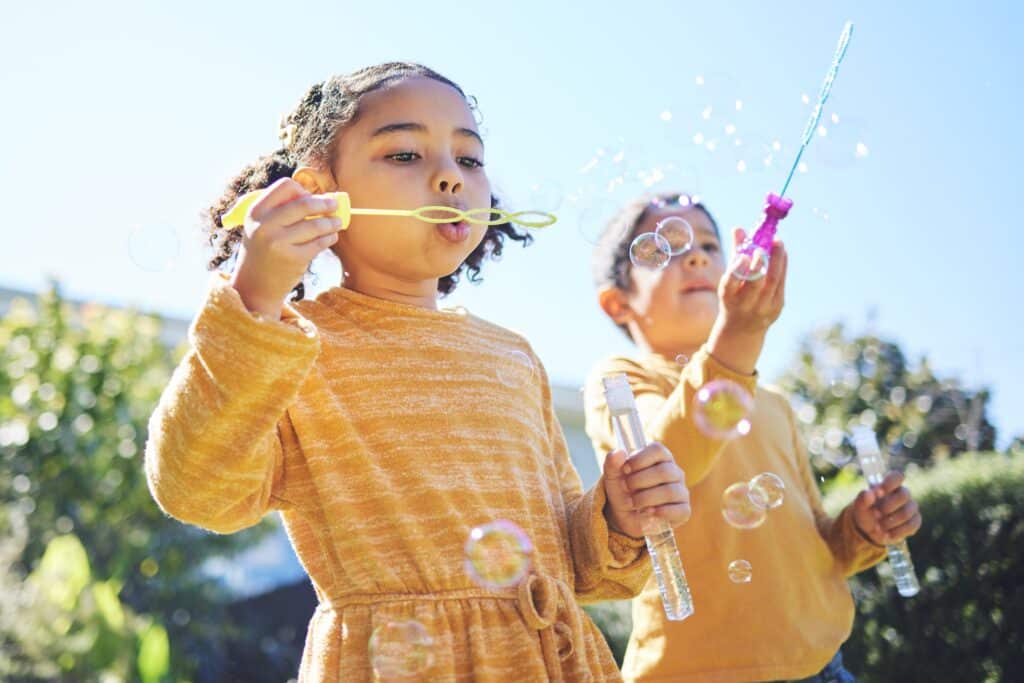Kinderen van 10-12 jaar spelen buiten met bellenblaas in de zon, voorbeeld van actief buitenspeelgoed