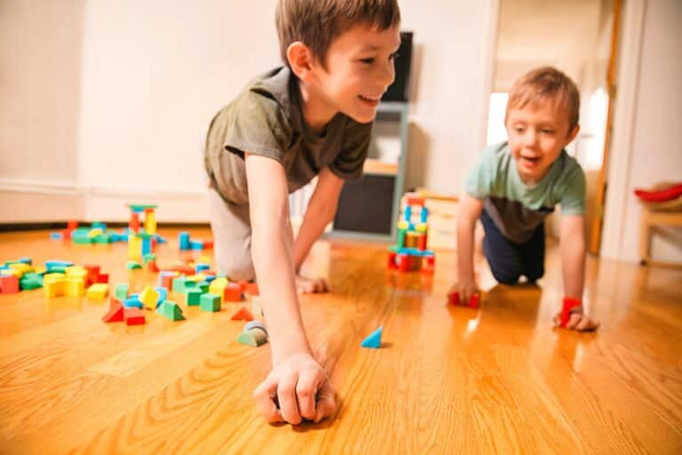 Twee kinderen spelen lachend met kleurrijke bouwstenen op een houten vloer