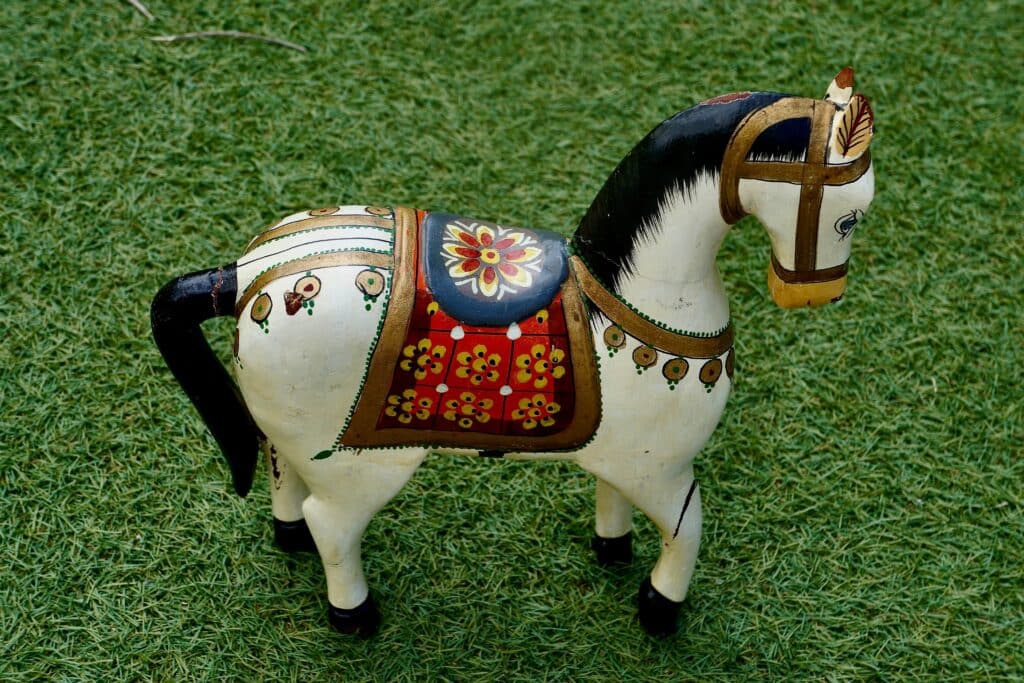 Een handbeschilderd houten paard met kleurrijke patronen staat op groen gras en toont traditionele details.